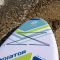 deska sup Gladiator Origin 10.6 – detal dziobu na kamienistej plaży, bagażnik z elastycznymi linkami