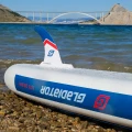 pompowana deska sup Gladiator Origin 10.8 Rental – statecznik i bok deski przy brzegu, logo na burcie, ujęcie na wodzie