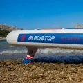 Gladiator Origin 10.8 Rental – logo Gladiator i napis 10’8 Origin na burcie, statecznik w płytkiej wodzie, ujęcie przy plaży