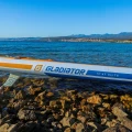 Gladiator Elite 12'6T – detal burty z napisem Gladiator, deska SUP na kamienistym brzegu